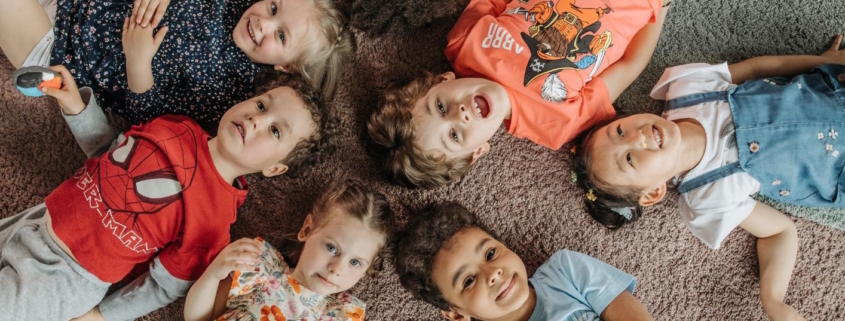 Kinder die gutgelaunt sternförmig im Kreis liegen